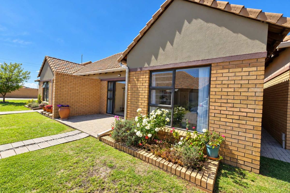 A well-maintained rear exterior view featuring a brick facade, tiled roof, paved patio area, and a landscaped brick garden bed.