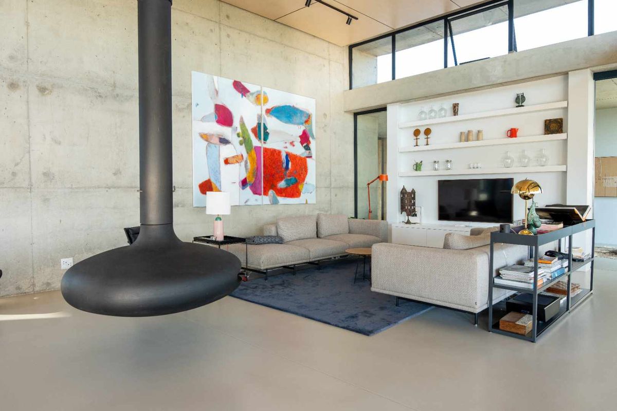 Spacious modern living area featuring exposed concrete walls, high ceilings with clerestory windows, and a striking suspended fireplace.
