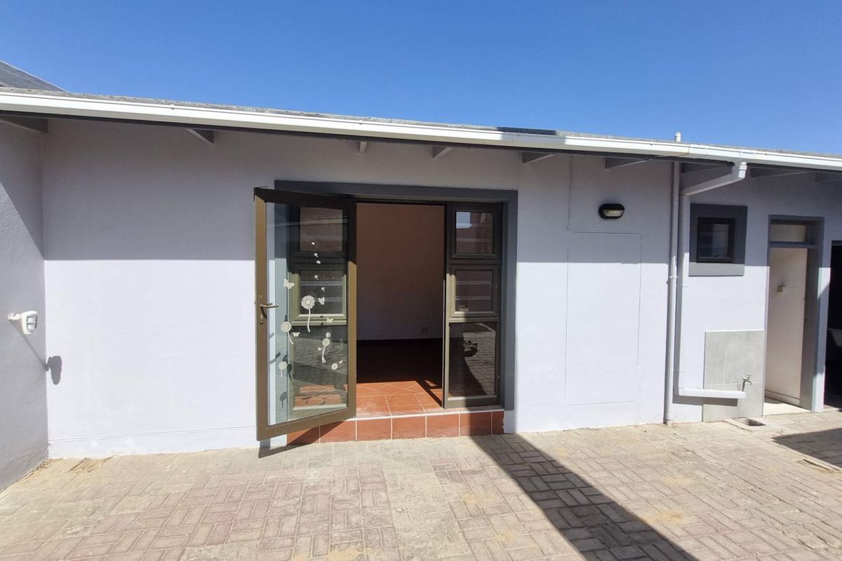 Rear exterior view featuring a paved patio area, terracotta tiled threshold, and aluminium framed glass doors leading into the property.