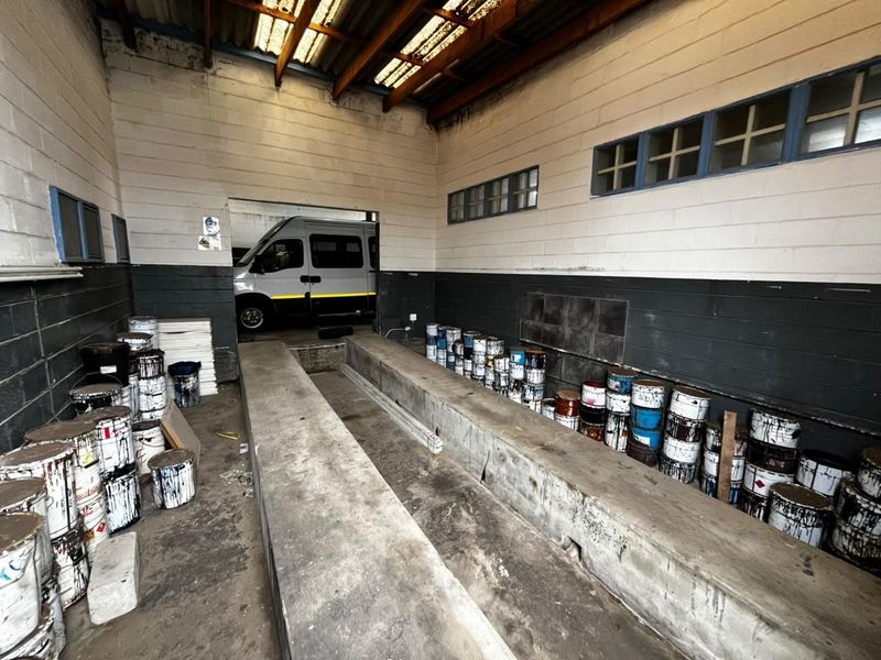 Industrial garage space featuring a built-in concrete inspection pit, exposed roof trusses, and high-level windows, suitable for automotive maintenance or workshop use.
