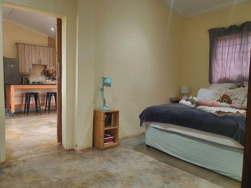 A bedroom with polished concrete floors and a view into an adjacent kitchen area featuring wooden cabinetry and a central island.
