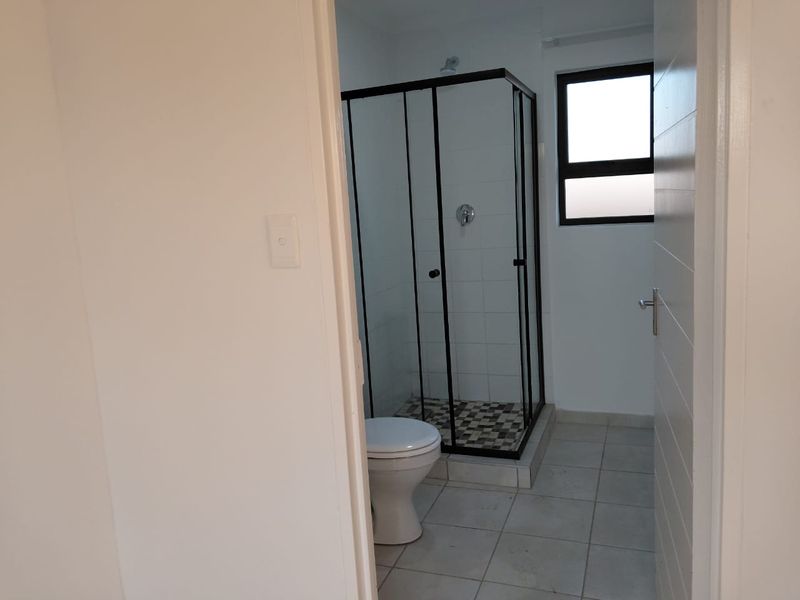 A clean, functional bathroom featuring a modern shower enclosure with black framing, a white toilet, and neutral floor tiling.