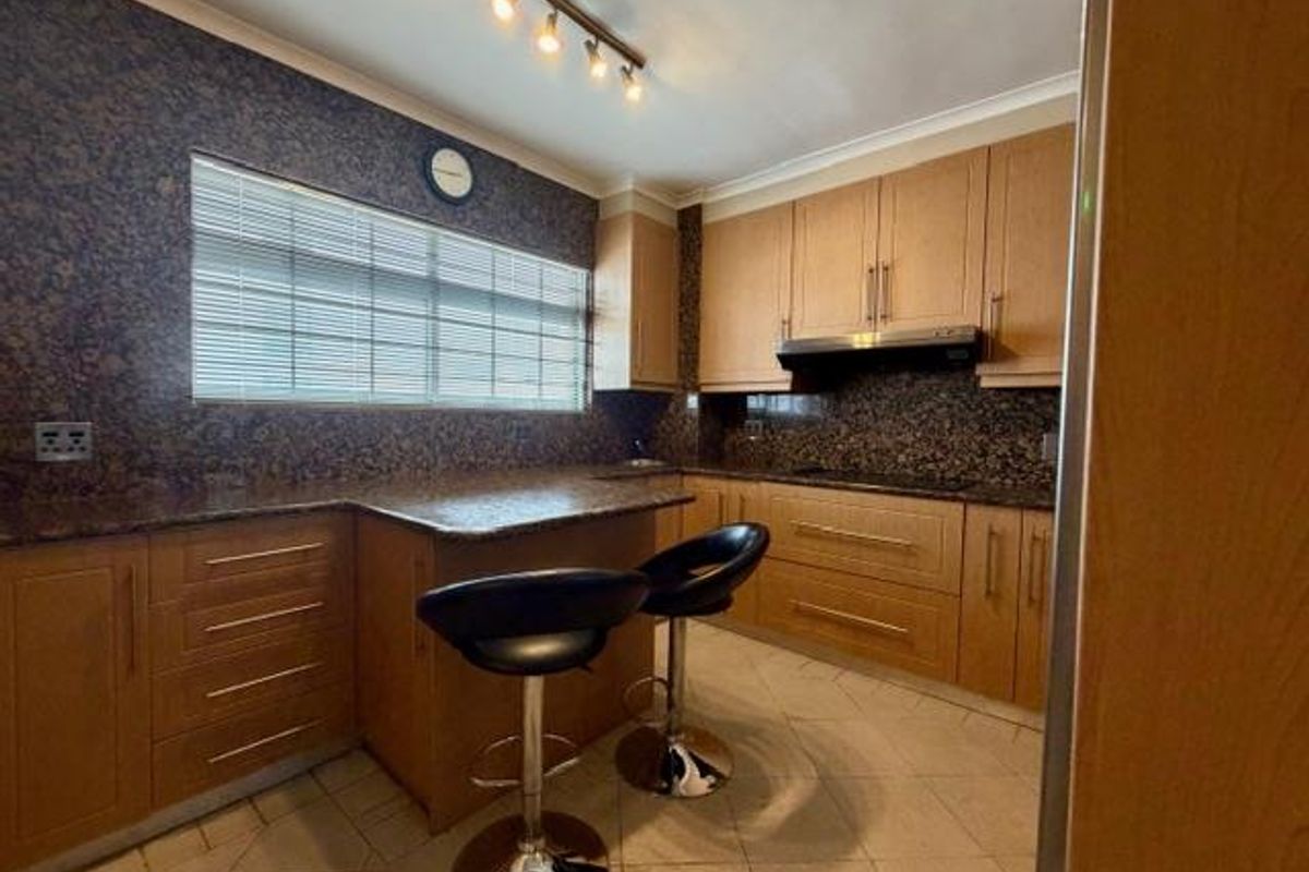 A functional kitchen featuring wooden cabinetry, granite countertops, a built-in hob with extractor fan, and tiled flooring with a breakfast bar area.