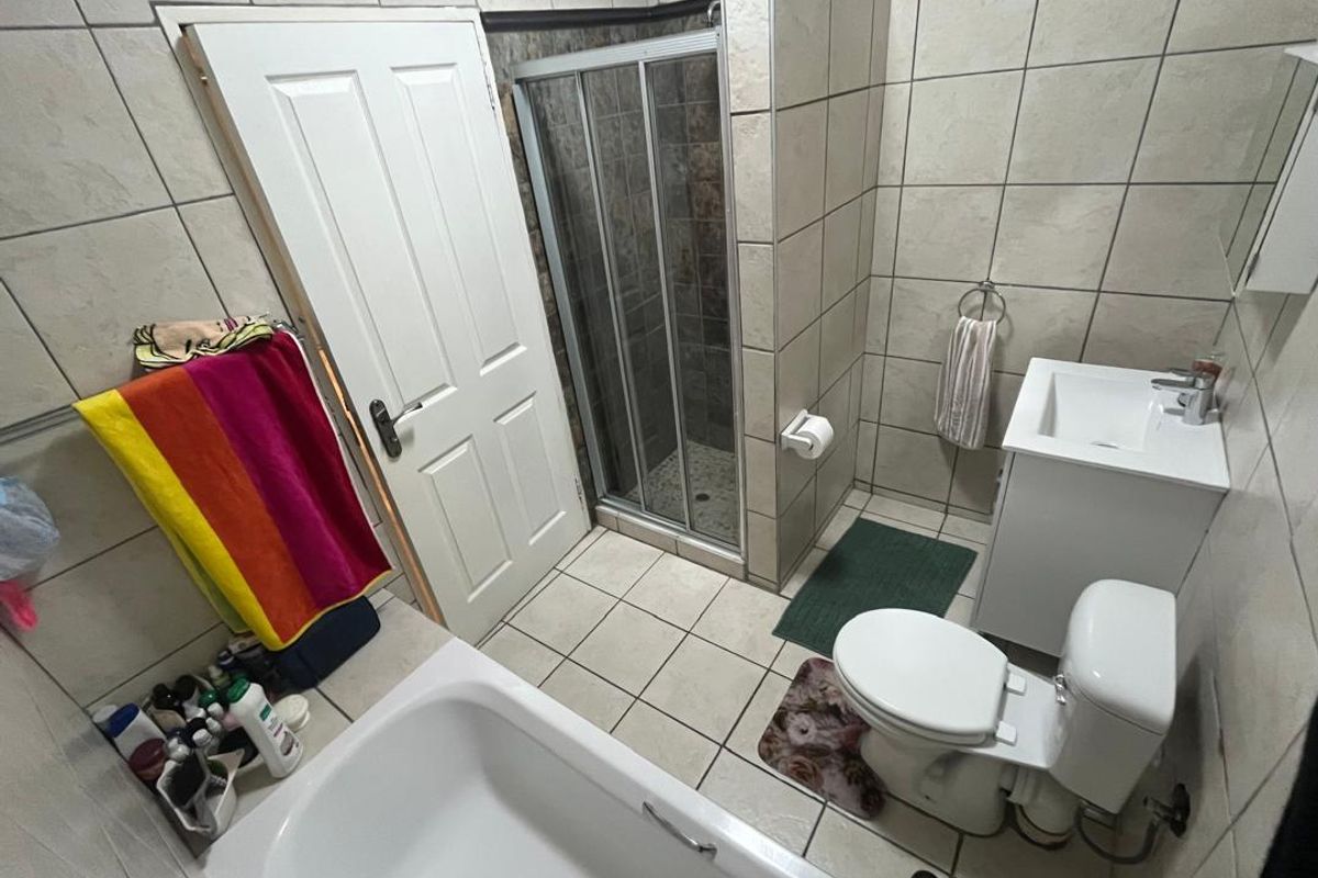 A functional bathroom featuring a shower enclosure, bathtub, toilet, and vanity basin with neutral wall and floor tiling.