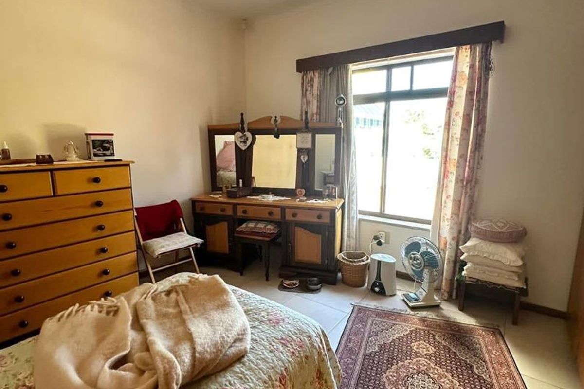 A bedroom featuring tiled flooring, a large window with curtain rails, and a central ceiling light fixture.