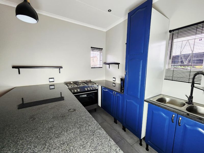 A clean, modern kitchen featuring blue cabinetry, granite countertops, a gas stove with oven, and a double basin sink with black fixtures.