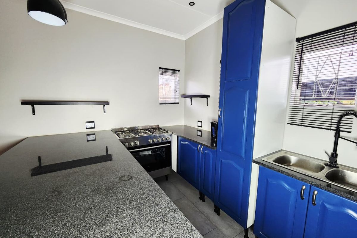 A clean, modern kitchen featuring blue cabinetry, granite countertops, a gas stove with oven, and a double basin sink with black fixtures.