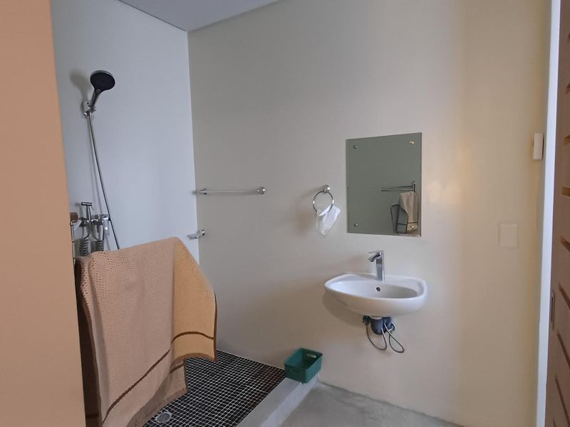 A functional bathroom featuring a wall-mounted basin, shower area with tiled flooring, and basic fixtures. The space is clean and ready for minor updates.