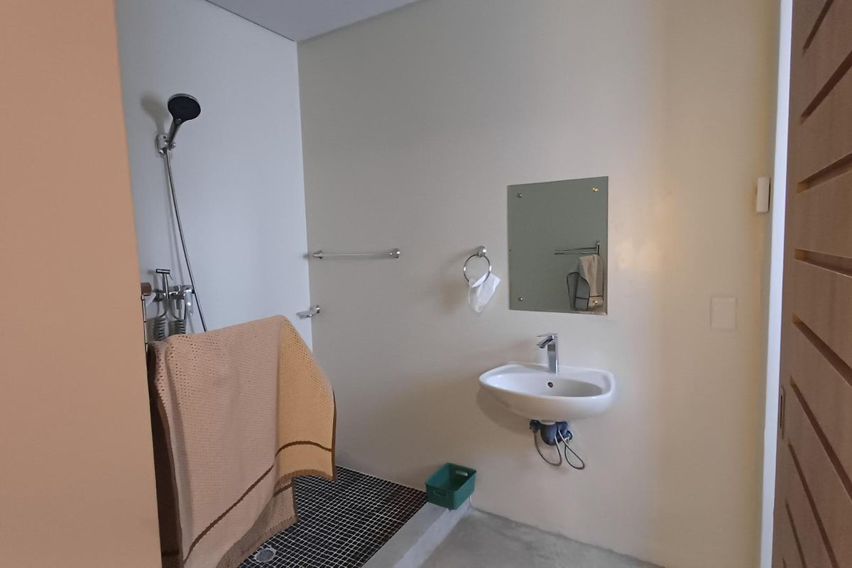 A functional bathroom featuring a wall-mounted basin, shower area with tiled flooring, and basic fixtures. The space is clean and ready for minor updates.