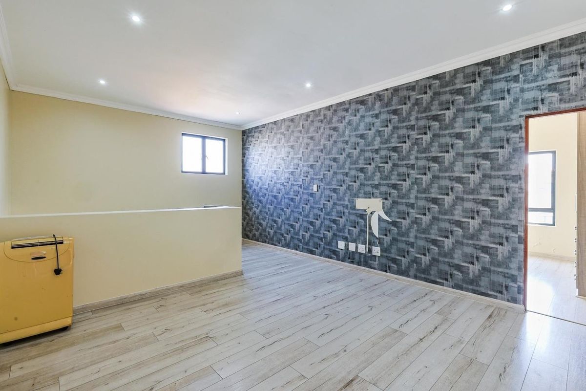 A spacious living area featuring modern wood-look laminate flooring, recessed ceiling lighting, and a striking patterned feature wall.
