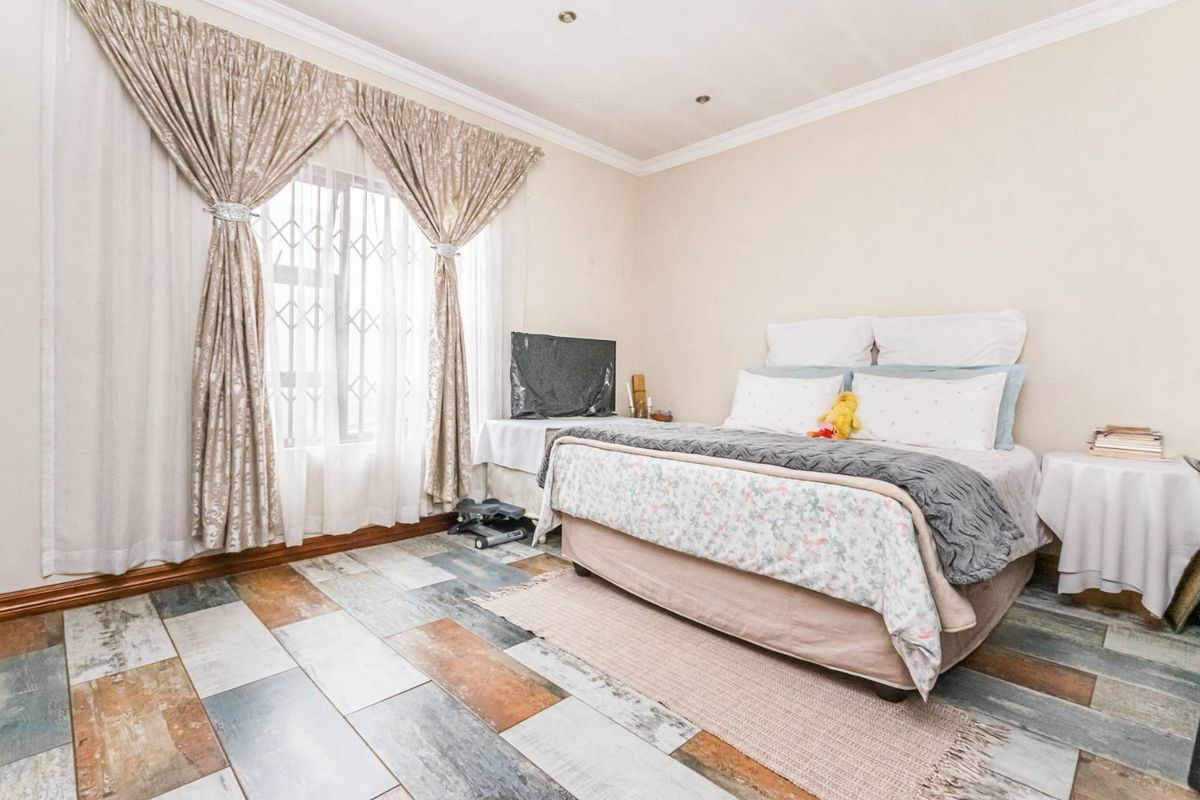 A well-lit bedroom featuring multi-toned wood-look tile flooring, crown molding, and a window fitted with security bars.