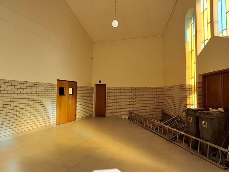 A spacious, high-ceilinged interior area featuring brick wall accents, large stained glass windows, and timber doors, currently used as a utility or storage space.
