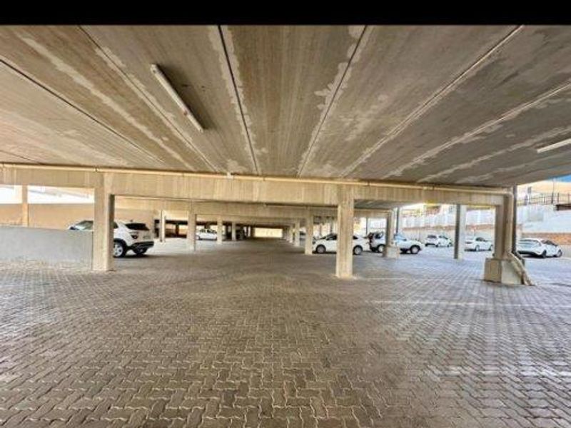 A covered parking garage area featuring concrete structural pillars, a concrete ceiling, and paved flooring.