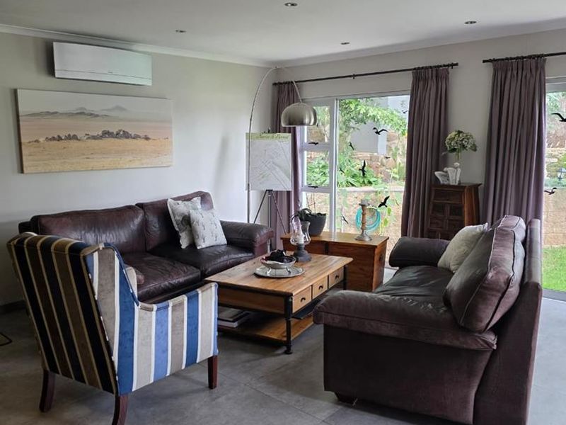 A comfortable living room featuring large format floor tiles, recessed lighting, and a wall-mounted air conditioning unit with direct access to the garden.
