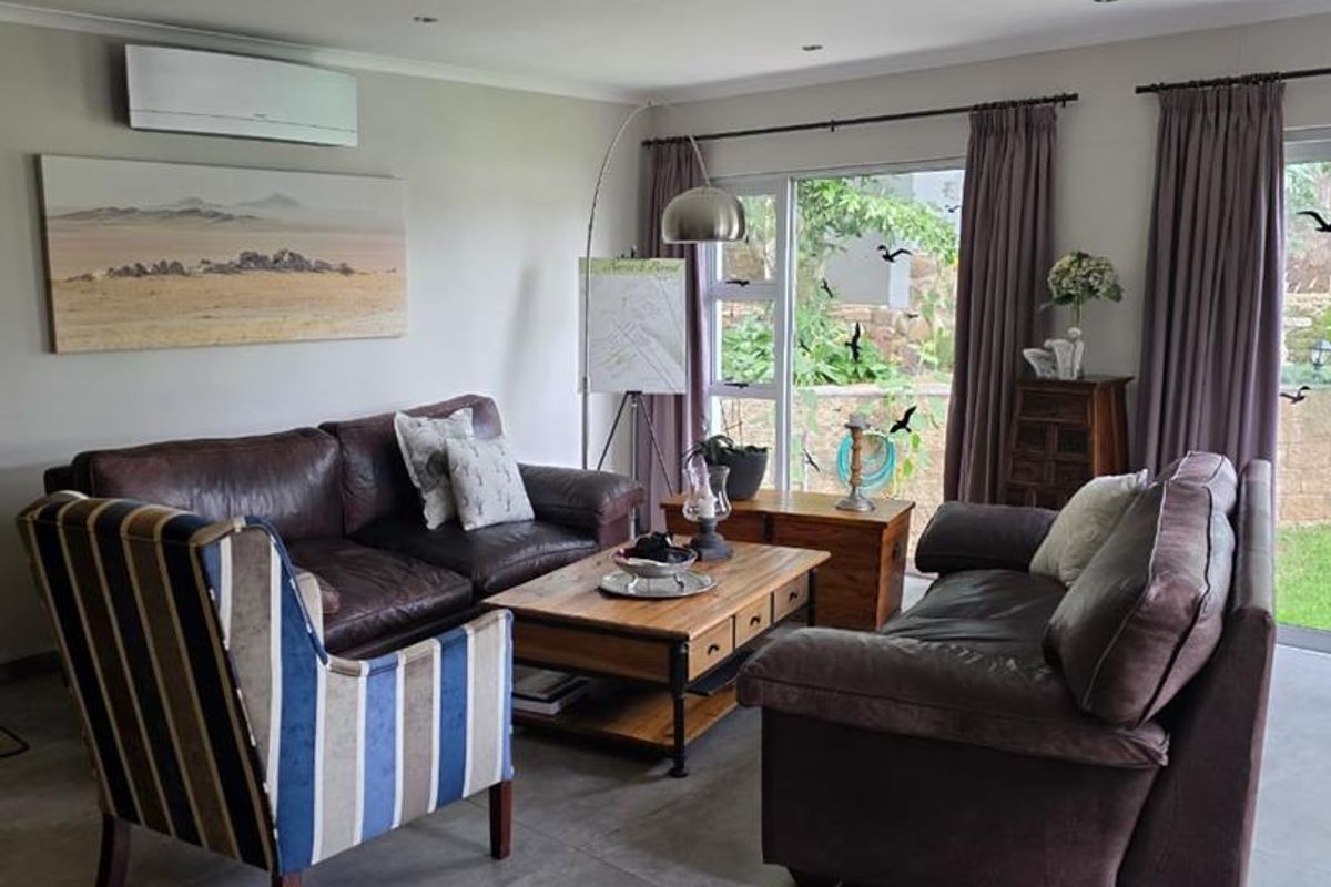 A comfortable living room featuring large format floor tiles, recessed lighting, and a wall-mounted air conditioning unit with direct access to the garden.