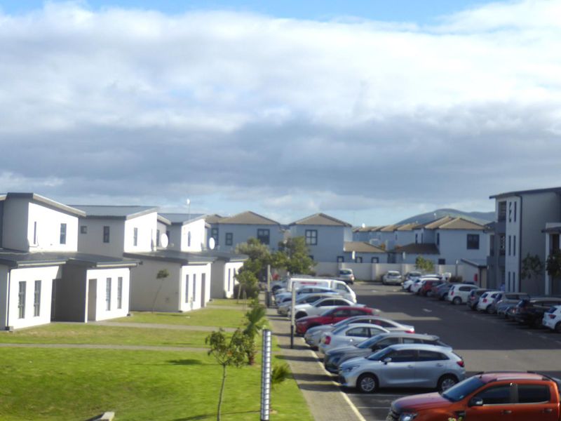 A view of the residential complex street, featuring paved parking areas, landscaped lawns, and multiple modern residential units.