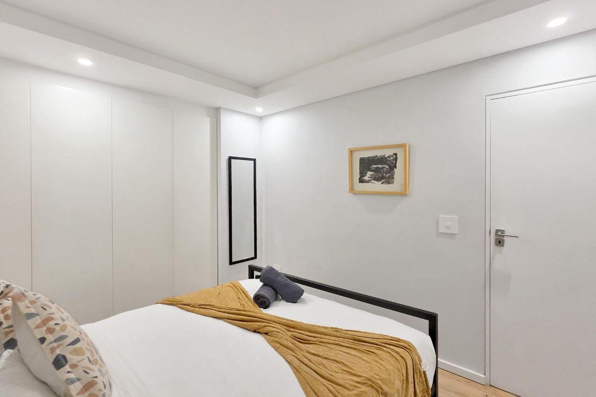 A clean, modern bedroom featuring built-in floor-to-ceiling wardrobes, recessed ceiling lighting, and light wood-look flooring.