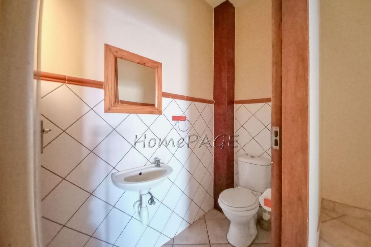 A compact guest bathroom featuring a wall-mounted basin, a standard toilet, and diamond-patterned wall tiles.