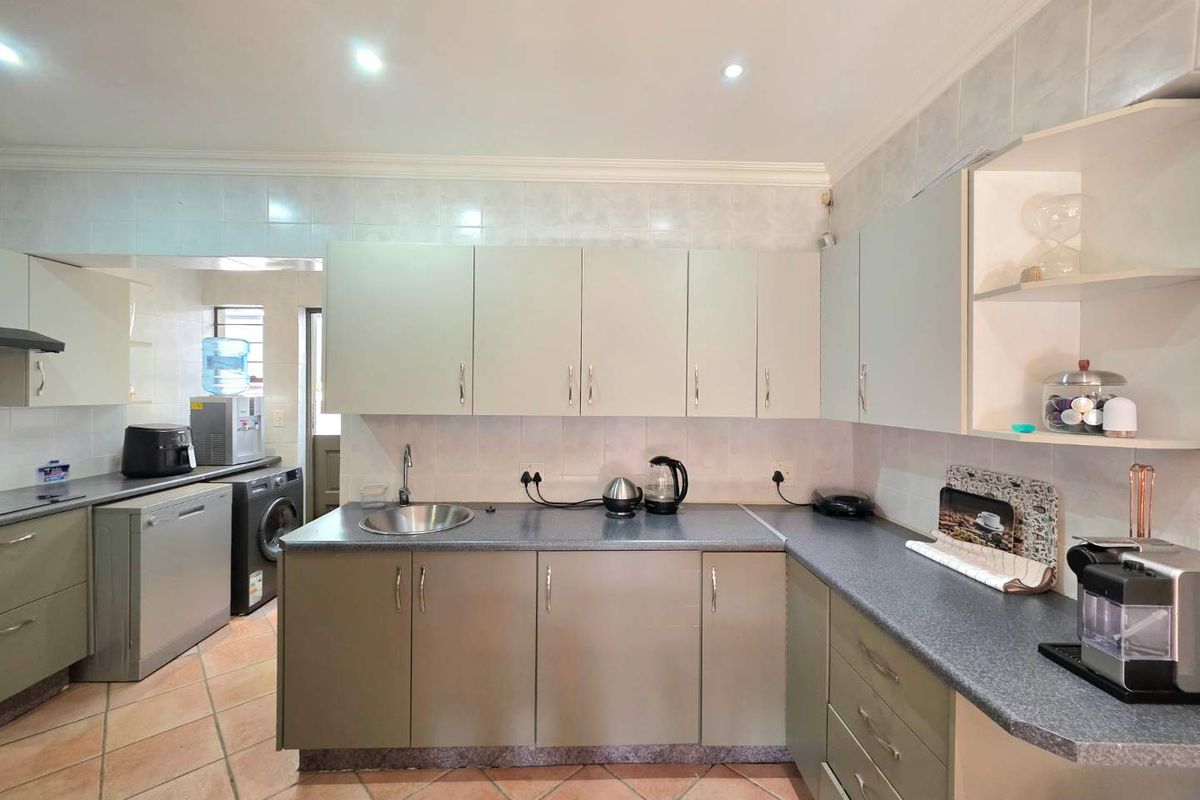 Functional kitchen featuring laminate countertops, ample cabinetry, tiled splashbacks, and a dedicated scullery area with laundry plumbing connections.