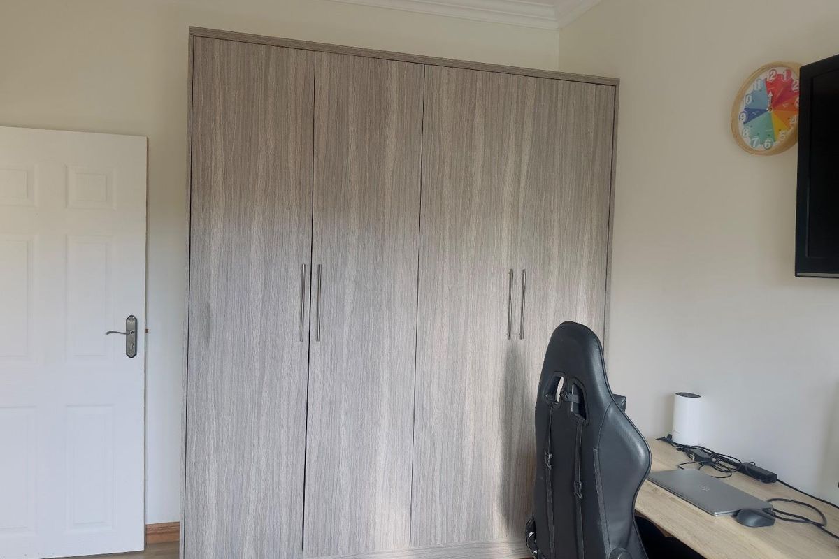 A bedroom featuring built-in floor-to-ceiling wardrobes with a modern wood-grain finish and crown molding detail.