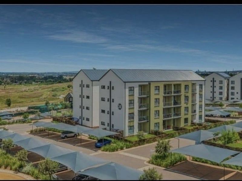 Aerial view of a modern multi-story apartment complex featuring covered parking bays and landscaped grounds in a suburban setting.