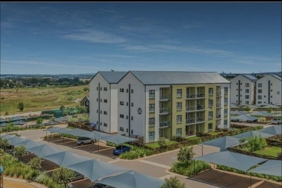 Aerial view of a modern multi-story apartment complex featuring covered parking bays and landscaped grounds in a suburban setting.