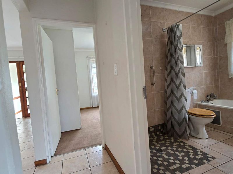 A functional bathroom featuring a bathtub, shower area with grab rails, and neutral wall tiling, adjacent to a hallway and bedroom entrance.