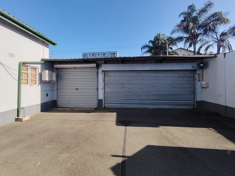 Exterior view of a commercial office property featuring a double garage with roller shutter doors and an asphalt driveway.