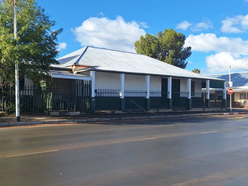 Street-facing view of an industrial property featuring a corrugated metal roof, a covered veranda with support columns, and secure perimeter metal fencing.