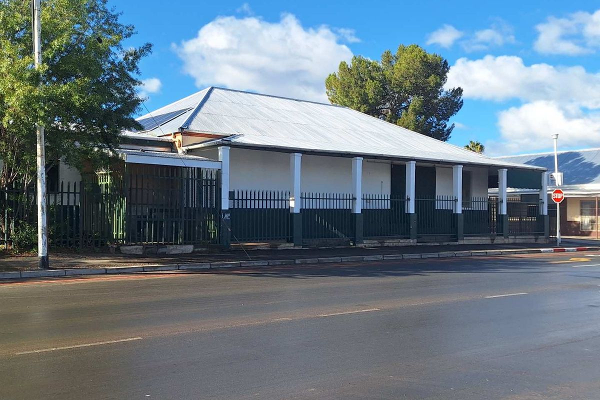 Street-facing view of an industrial property featuring a corrugated metal roof, a covered veranda with support columns, and secure perimeter metal fencing.