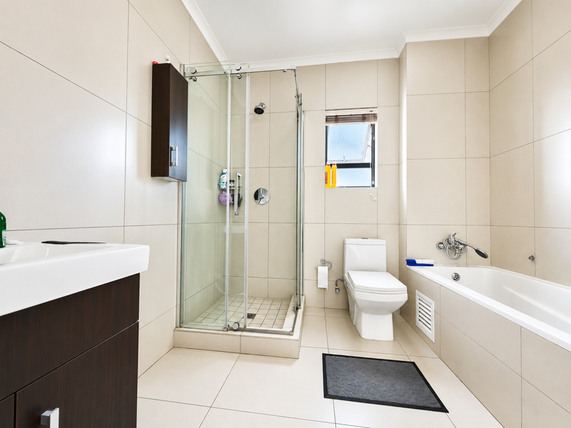 Modern bathroom featuring a glass shower enclosure, a built-in bathtub, a vanity unit, and neutral floor-to-ceiling wall tiles.