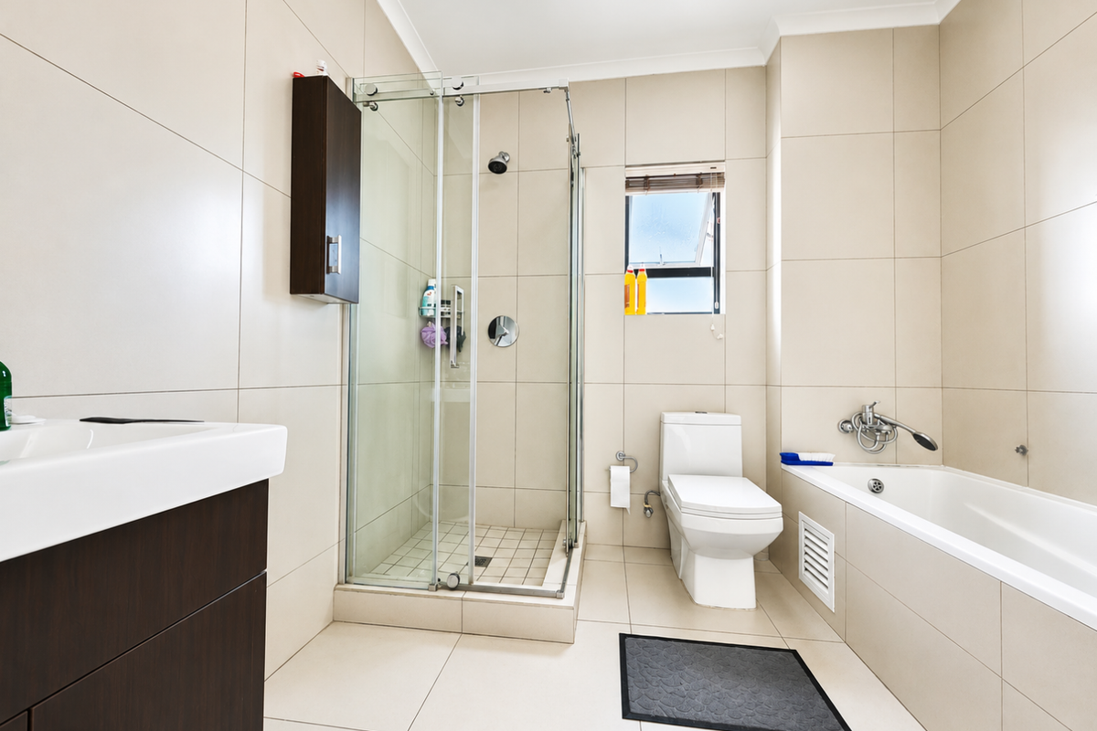 Modern bathroom featuring a glass shower enclosure, a built-in bathtub, a vanity unit, and neutral floor-to-ceiling wall tiles.