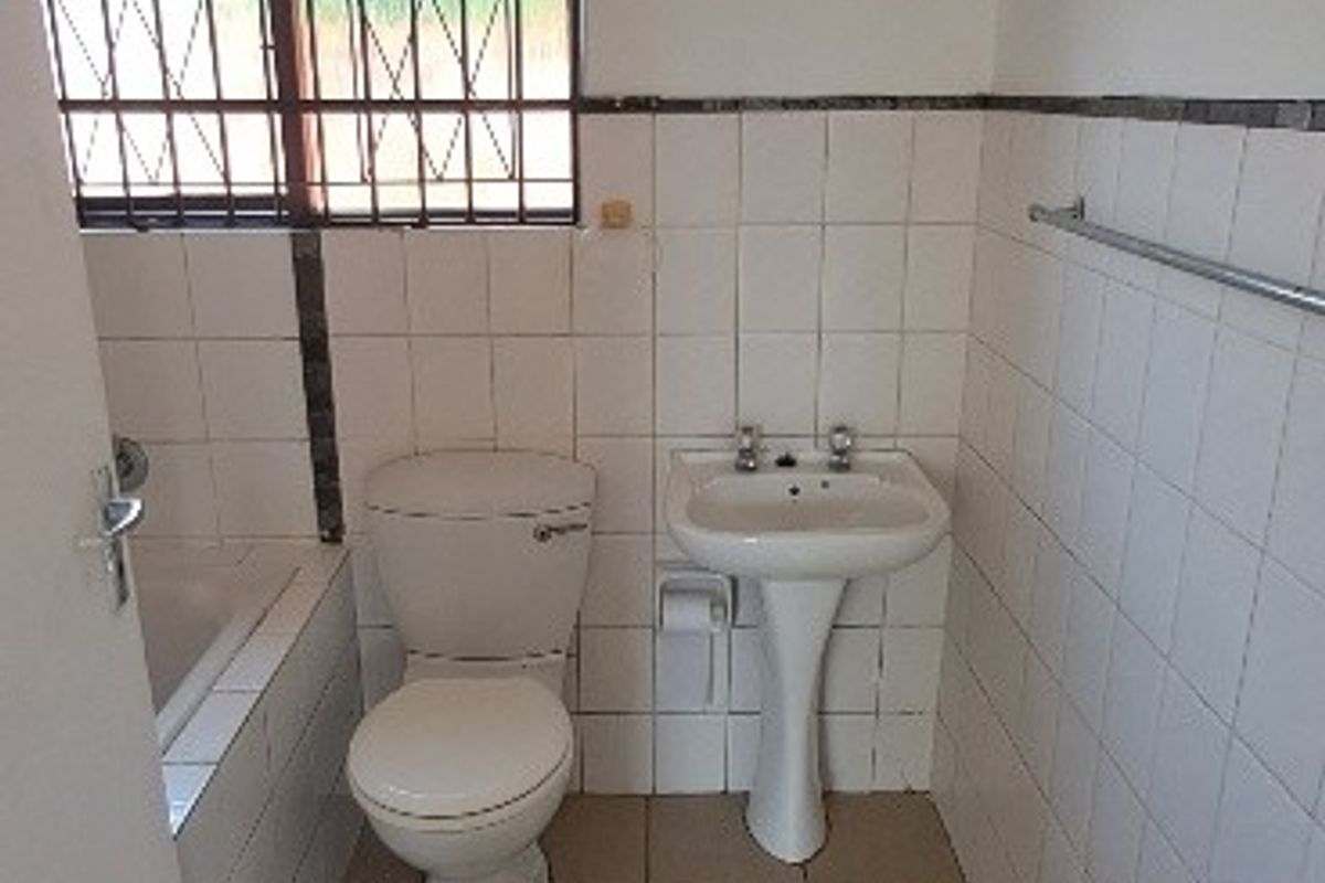 A functional bathroom featuring a pedestal basin, toilet, and built-in bathtub with tiled finishes and security bars on the window.