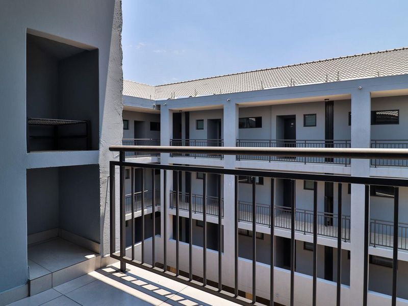 A private balcony featuring tiled flooring, a built-in braai, and a metal balustrade, overlooking the apartment complex courtyard.