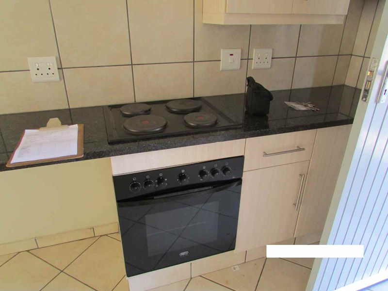A functional kitchen area featuring a built-in oven, electric hob, granite countertops, and tiled backsplash with ample cabinetry.