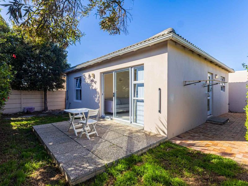 Rear view of the property featuring a paved patio area, sliding glass doors, and a well-maintained garden space.