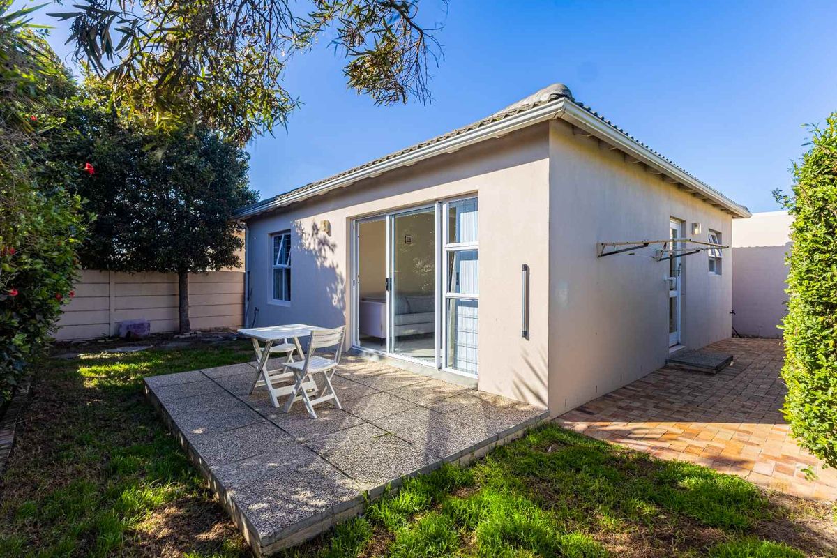 Rear view of the property featuring a paved patio area, sliding glass doors, and a well-maintained garden space.
