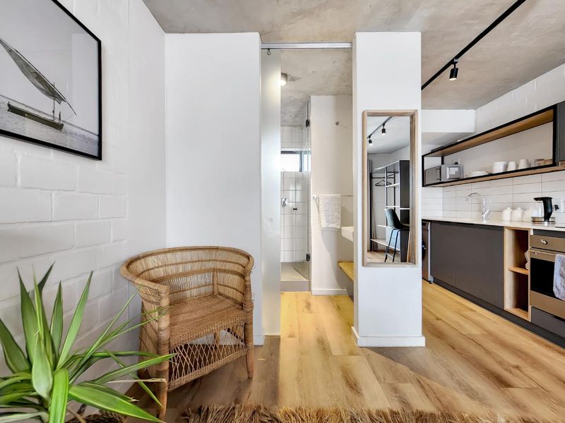 Modern open-plan apartment featuring an industrial-style exposed concrete ceiling, sleek kitchen cabinetry, timber flooring, and a contemporary bathroom with a walk-in shower.