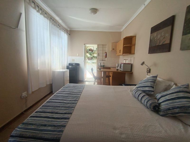 An open-plan guest room featuring a sleeping area and a compact kitchenette with built-in cabinetry and counter space, leading to an outdoor area.