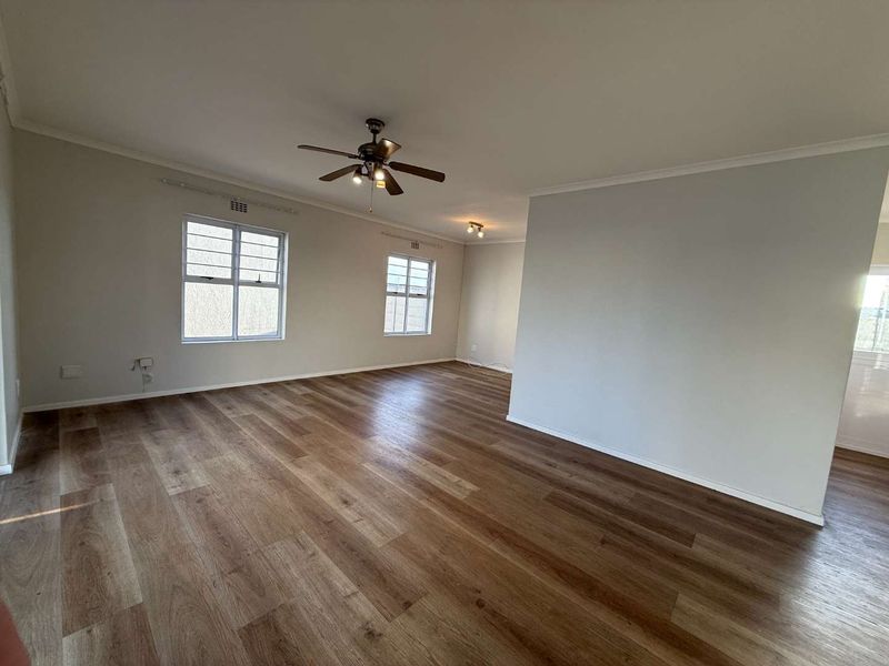A spacious, empty living area featuring modern laminate wood flooring, neutral walls, and a ceiling fan, offering a clean canvas for interior design.