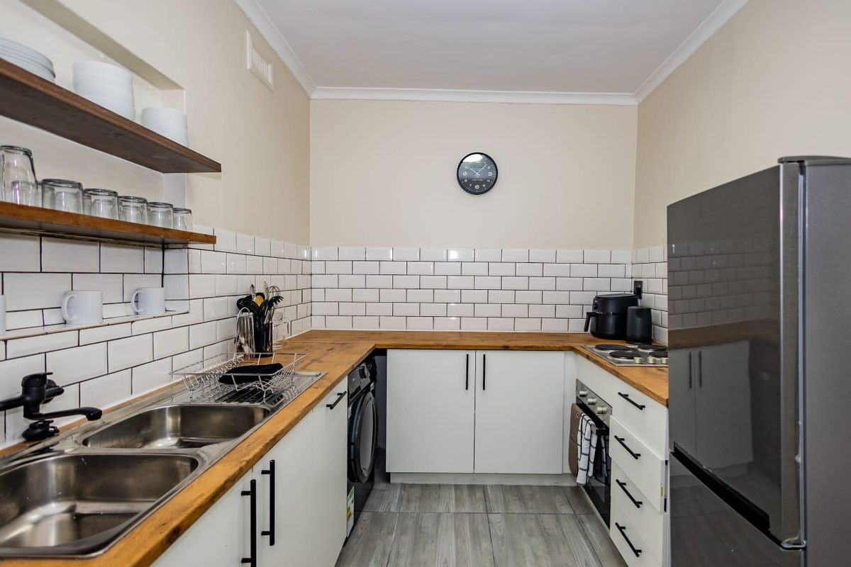 Compact kitchen featuring white cabinetry, subway tile backsplash, wooden countertops, double stainless steel sink, and integrated oven with hob.