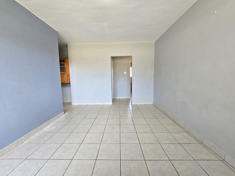 An empty, open-plan living area featuring neutral grey walls and ceramic tiled flooring, providing a blank canvas for interior design.