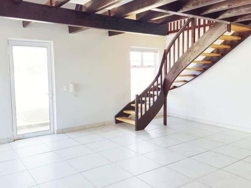 Spacious open-plan living area featuring exposed timber ceiling beams, a striking curved wooden staircase, and neutral tiled flooring with direct outdoor access.