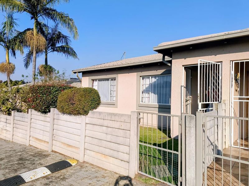 Front elevation of a townhouse featuring a precast concrete boundary wall, metal security gate, and tiled roof with paved driveway access.