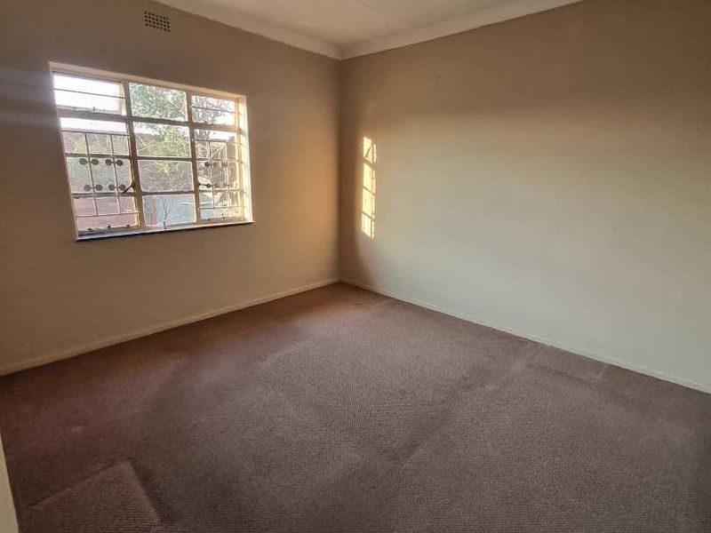 An empty bedroom featuring a steel-framed window, carpeted flooring, and a simple ceiling light fixture, ready for personalization.