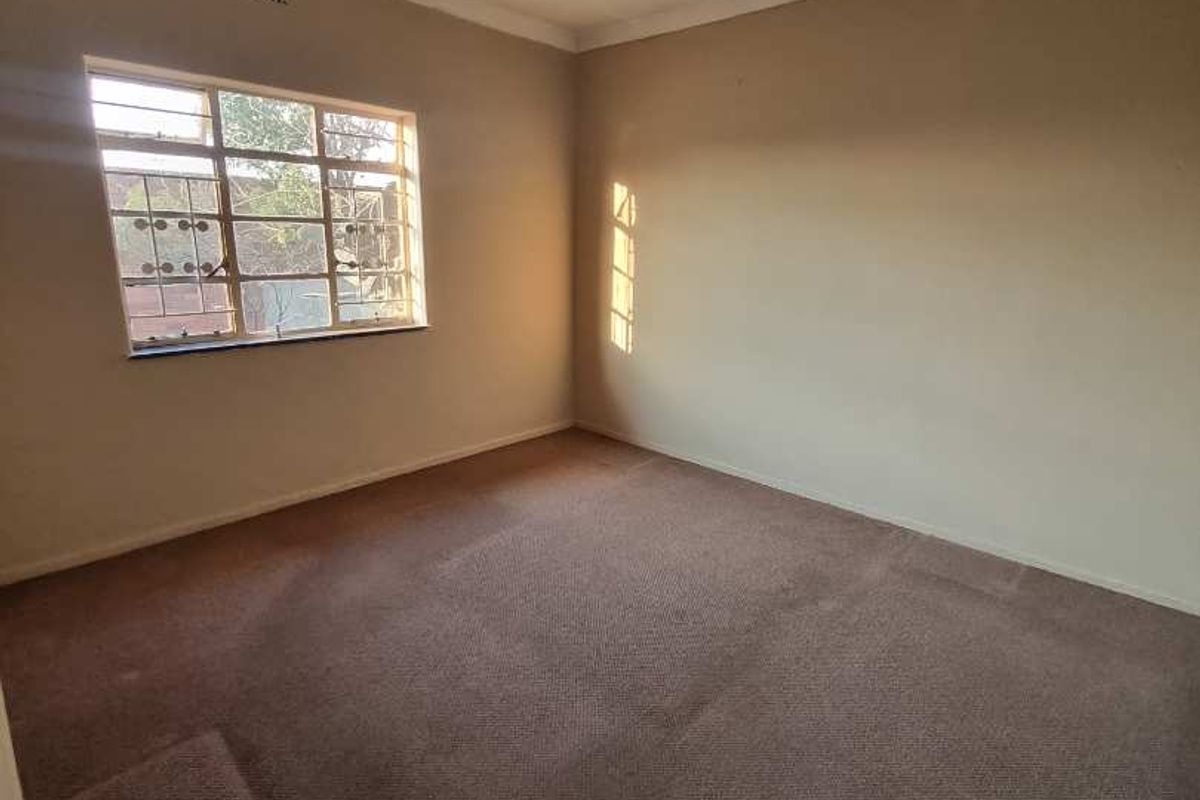An empty bedroom featuring a steel-framed window, carpeted flooring, and a simple ceiling light fixture, ready for personalization.