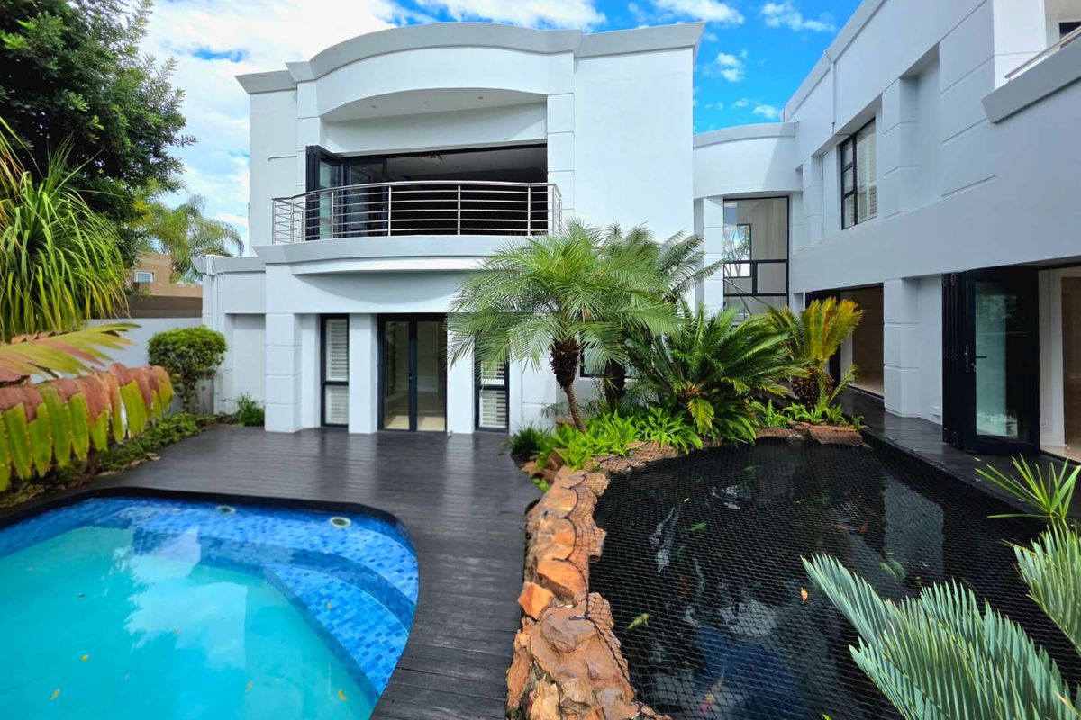 Rear exterior view featuring a modern swimming pool, a koi pond with stone edging, timber decking, and a balcony with stainless steel balustrades.