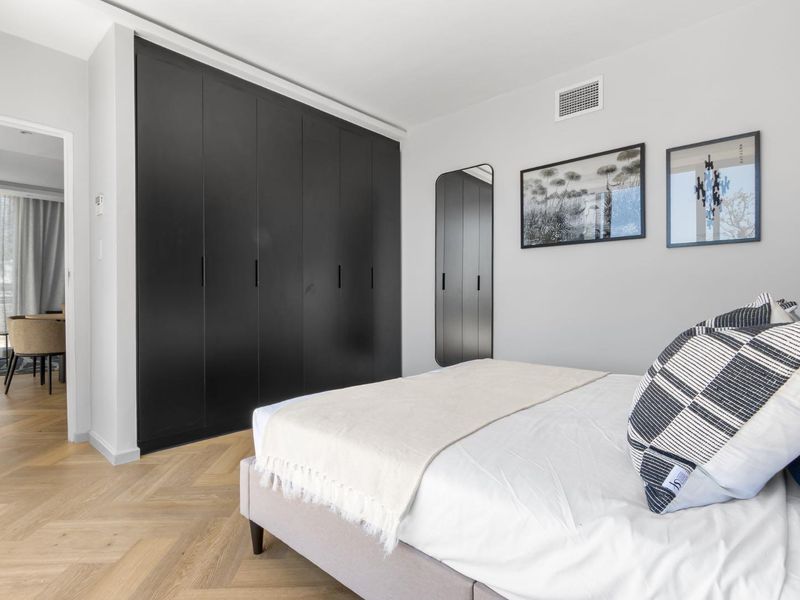 Modern bedroom featuring sleek black built-in cupboards, light herringbone timber flooring, and a neutral color palette.