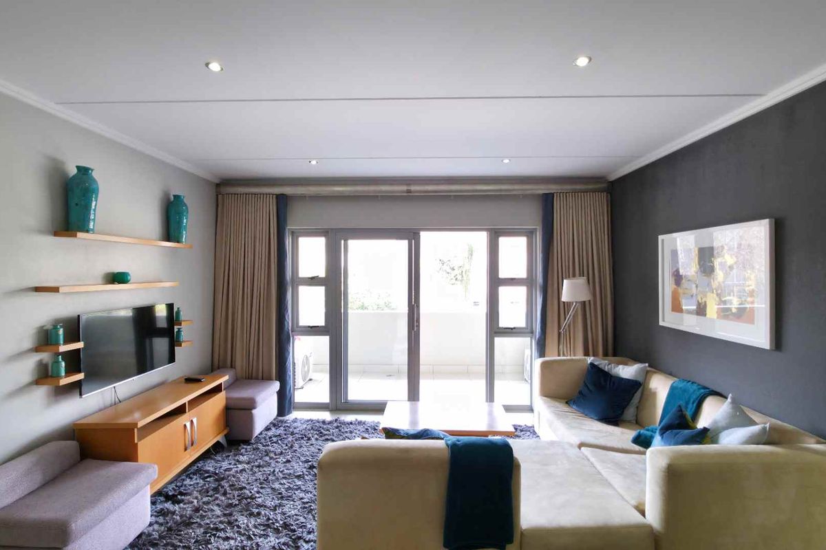 A well-maintained living room featuring recessed downlighting, modern grey accent walls, and large sliding glass doors providing access to an outdoor balcony.