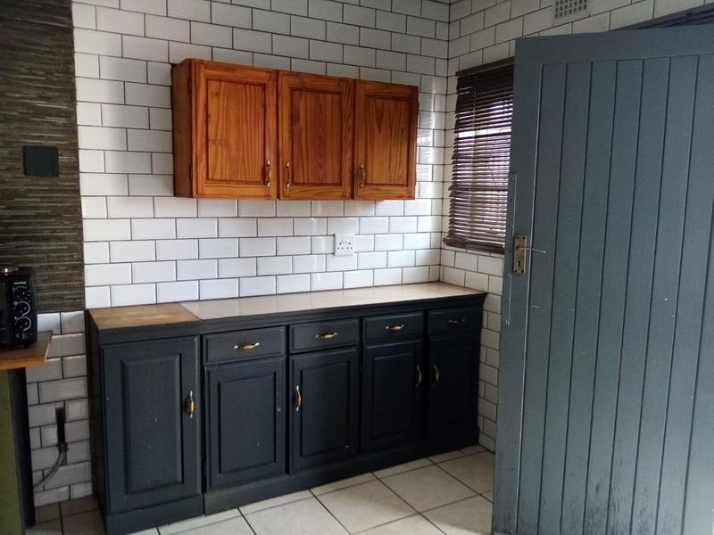 A kitchen area featuring a subway tile backsplash, wooden wall cabinets, and dark base cabinetry with tiled flooring.